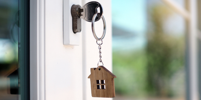 A silver key in a lock with a small wooden house on a keyring.
