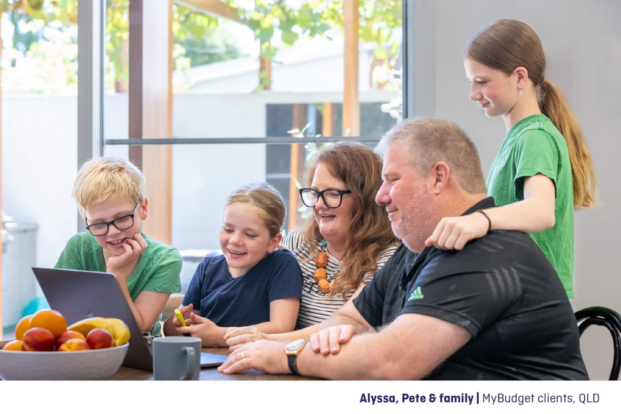 Alyssa and Pete, MyBudget clients, sit with their children at the dining table, reviewing their bills and discussing their budget. They smile as they work together, finding confidence and peace of mind with MyBudget’s support.