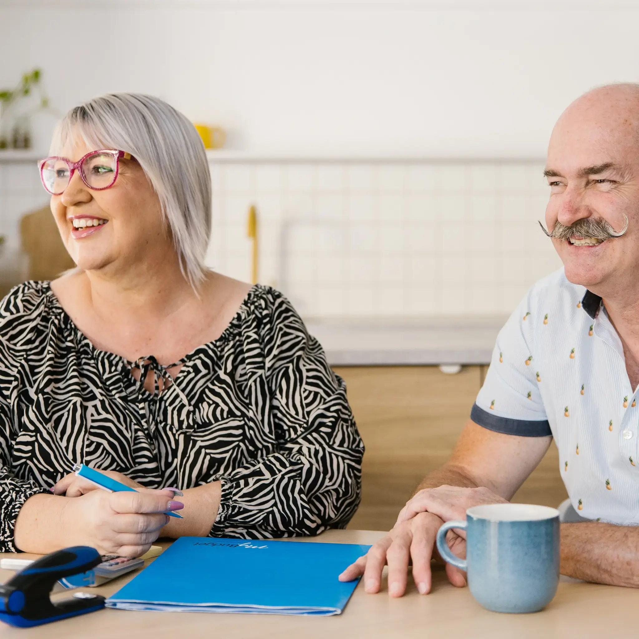 MyBudget clients Kylie and Scott at a table, discussing their budget planning and achieving financial goals in Australia.
