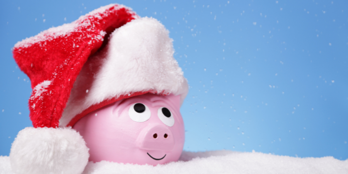 A piggy bank wearing a Christmas Santa hat sitting in fake snow: How much to save for Christmas