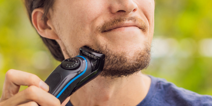 A man holding a beard trimmer to his face shaving.