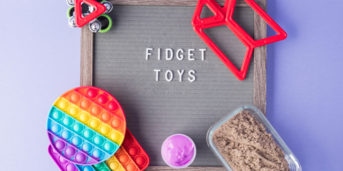 Fidget toys and sand in a container placed in the corners of a board that reads FIDGET TOYS in white letters: Stocking fillers for kids.