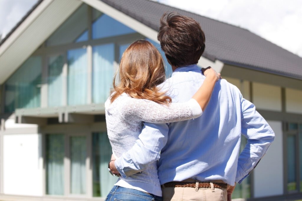 A man and woman hugging with their backs to the camera looking at a house - how to achieve financial goals.