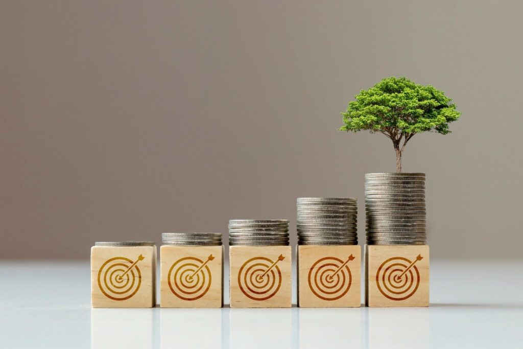 Give cube wooden blocks with arrows hitting targets painted on them, with stacks of silver coins ascending left to right and the last stack having a tree on top - building towards your new year financial goals.
