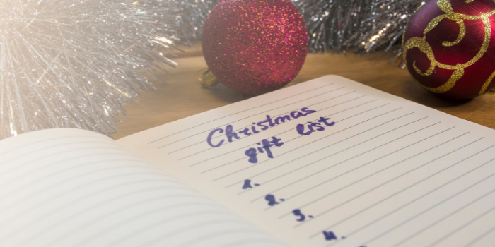 An open notepad with Christmas Gift List and dot point numbers written on it surround by Christmas baubles and tinsel: How to make a Christmas Budget