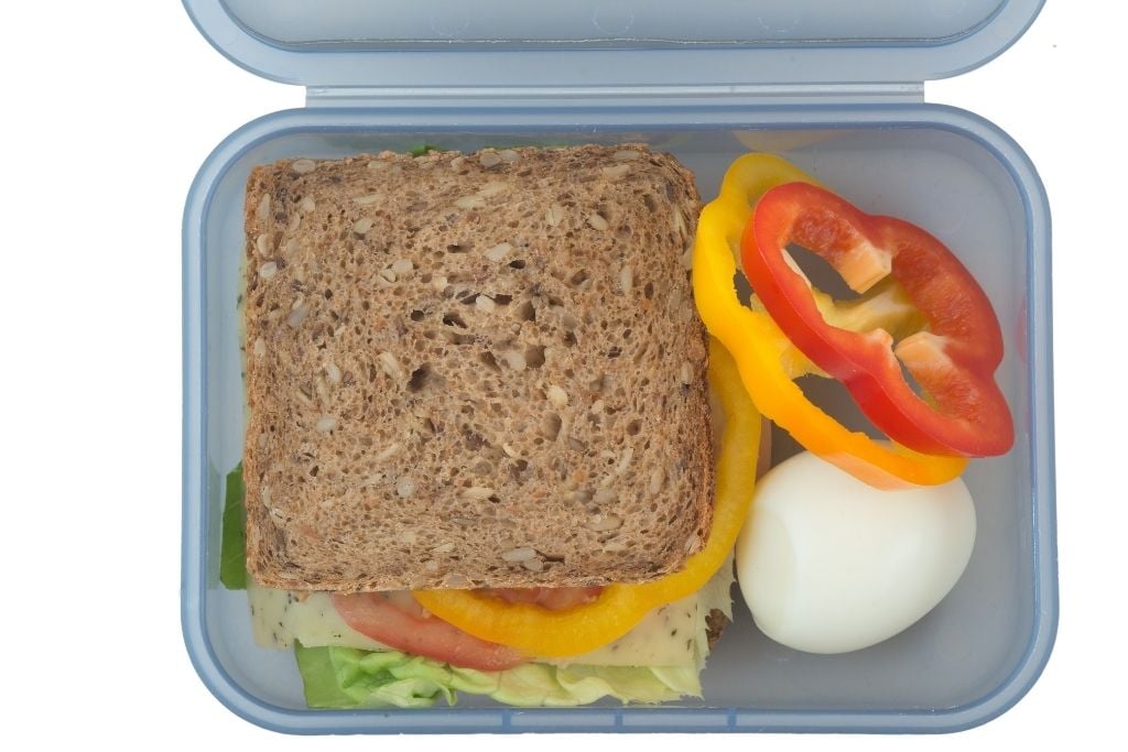 A salad sandwich on brown bread in a blue lunch box with some extra capsicum and a hard boiled egg on the side.