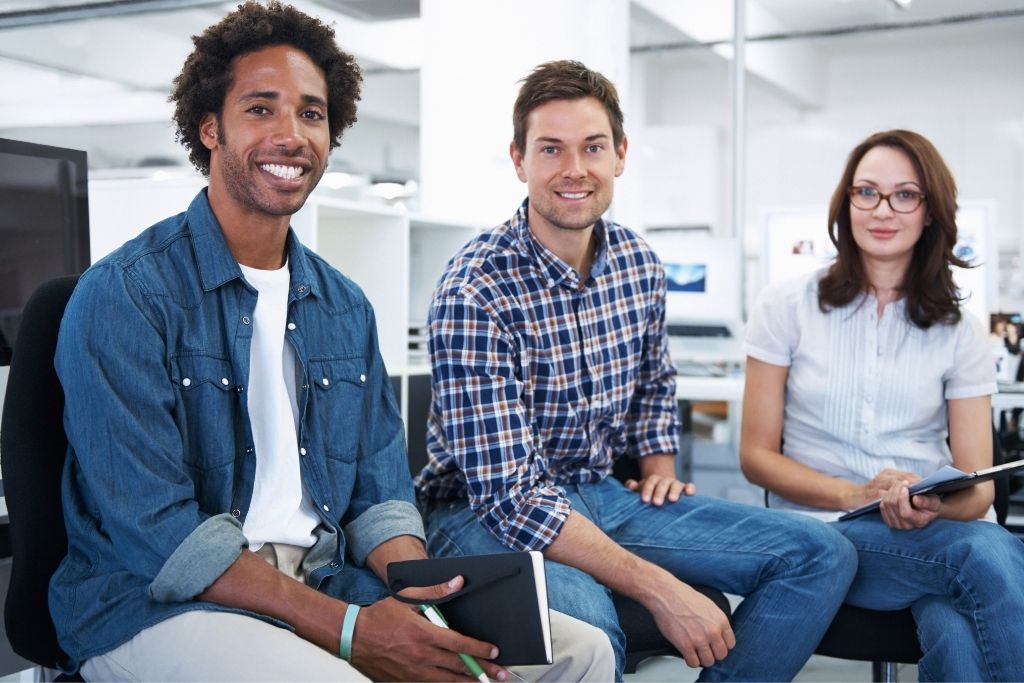 A man in a denim shirt, a man in a check shirt & a woman in a white shirt posed in a modern office - Start-up costs for a business