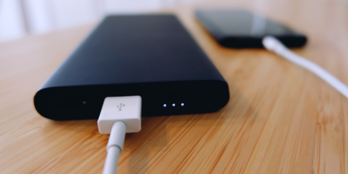 A black portable charger with a white cable plugged into a black phone in the background: Stocking fillers for men