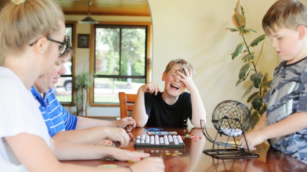 A mum and three kids playing bingo on the kitchen table