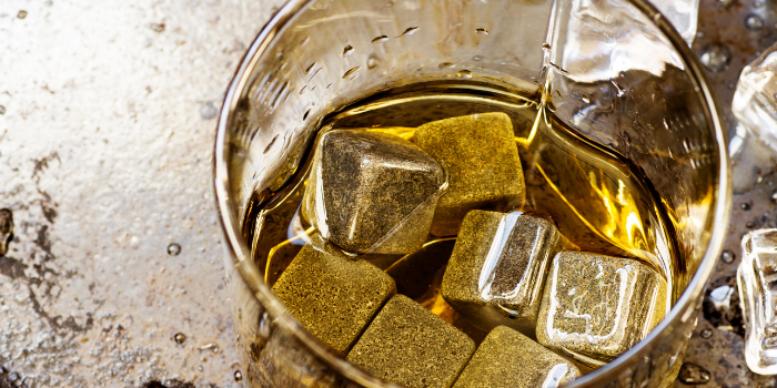 Seven whisky stones in a glass of scotch with ice cubs on the bench around it.