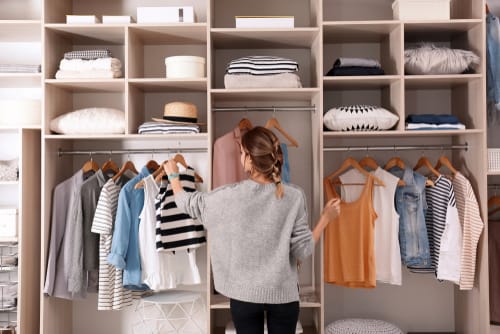 A woman is standing in front of a large wardrobe sorting looking for clothes to take out.