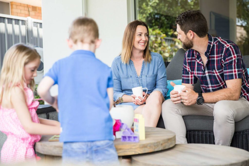 Mother, father, son and daughter sitting and standing in a living room having coffee