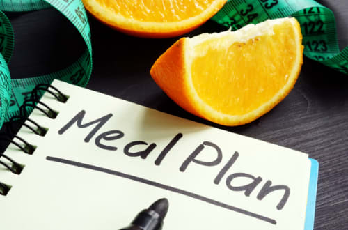 A sliced orange sits above a notebook with ‘Meal Plan’ written on it.