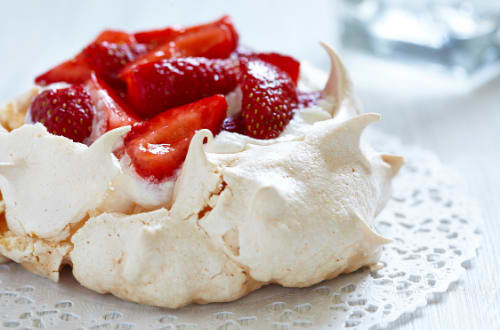 A close up shot of a freshly made pavlova with strawberries on top.