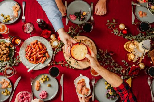 A person passes a dip to a person sitting opposite them at a crowded Christmas table on a budget.