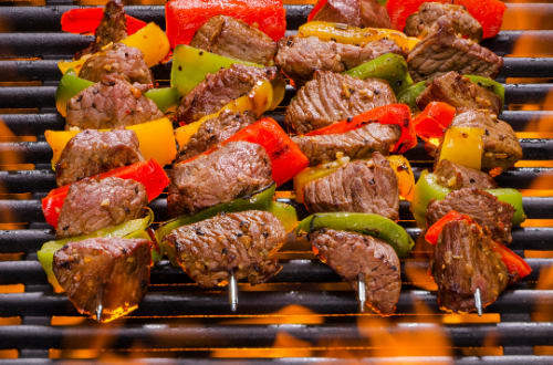Four beef kebabs with capsicum and season are flame grilled on top of a griddle plate.