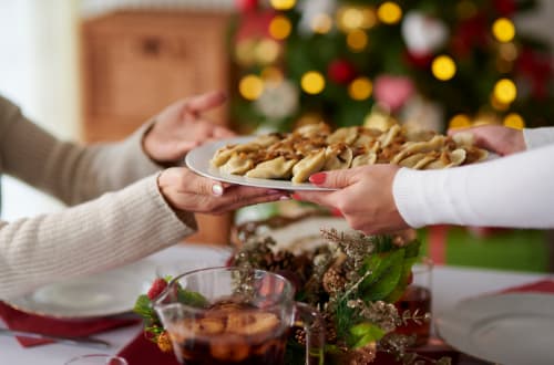 A person passes over a plate of dumplings to another person who are both sitting at a Christmas table on a budget