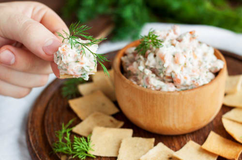 A person reaches for a salmon dip that sits atop a board full of crackers and dip.