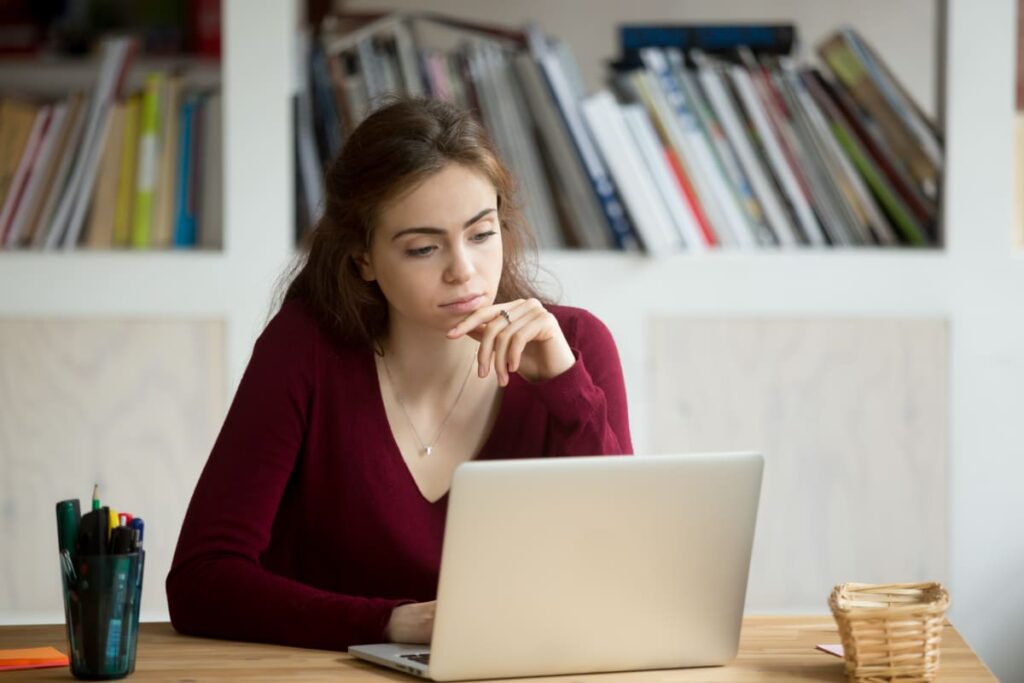 A young woman in a red jumper staring at her laptop in deep thought