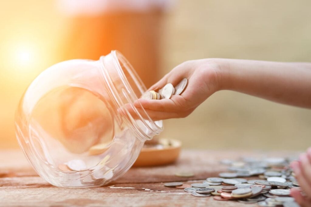 A person lays coins out on a table and slowly counts each one as they put their coins in a jar.