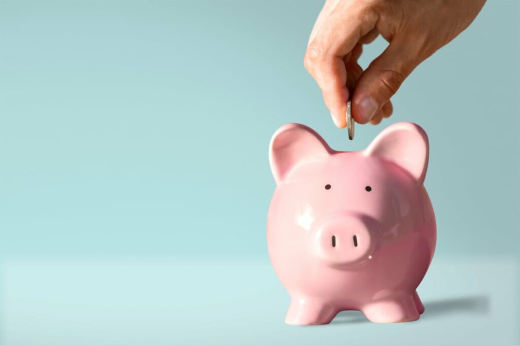 A person places one coin into a small piggybank.