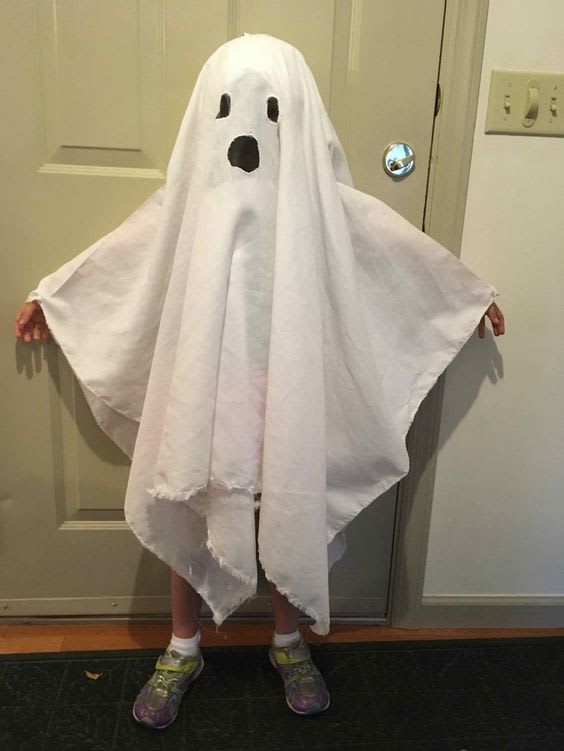 A young child wearing a white bed sheet with holes cut out like a ghost