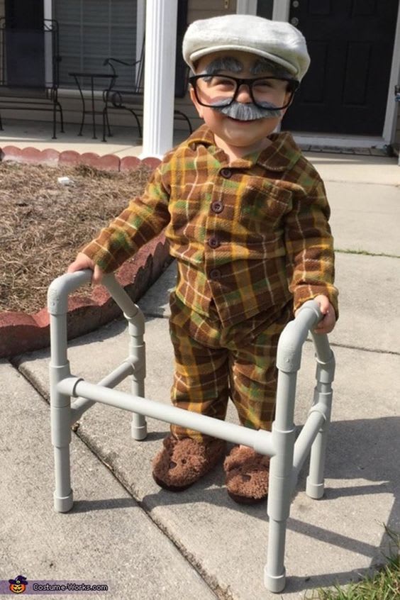A young toddler boy wearing pyjamas, a fake grey moustache & eyebrows, large glasses and a bureau hat, pushing around a walker made of pipes as cheap halloween costumes ideas