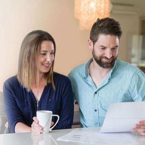 MyBudget clients Bec and Jarrad sitting at a table looking at a debt consolidation form.