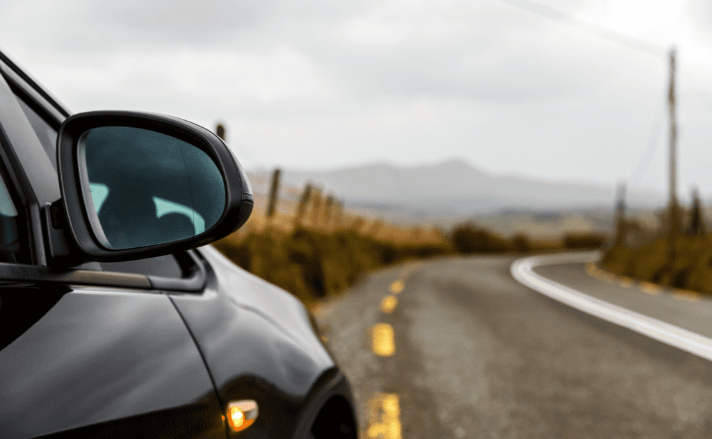 A close-up image of a car's side-view mirror with mountain ranges in the background.